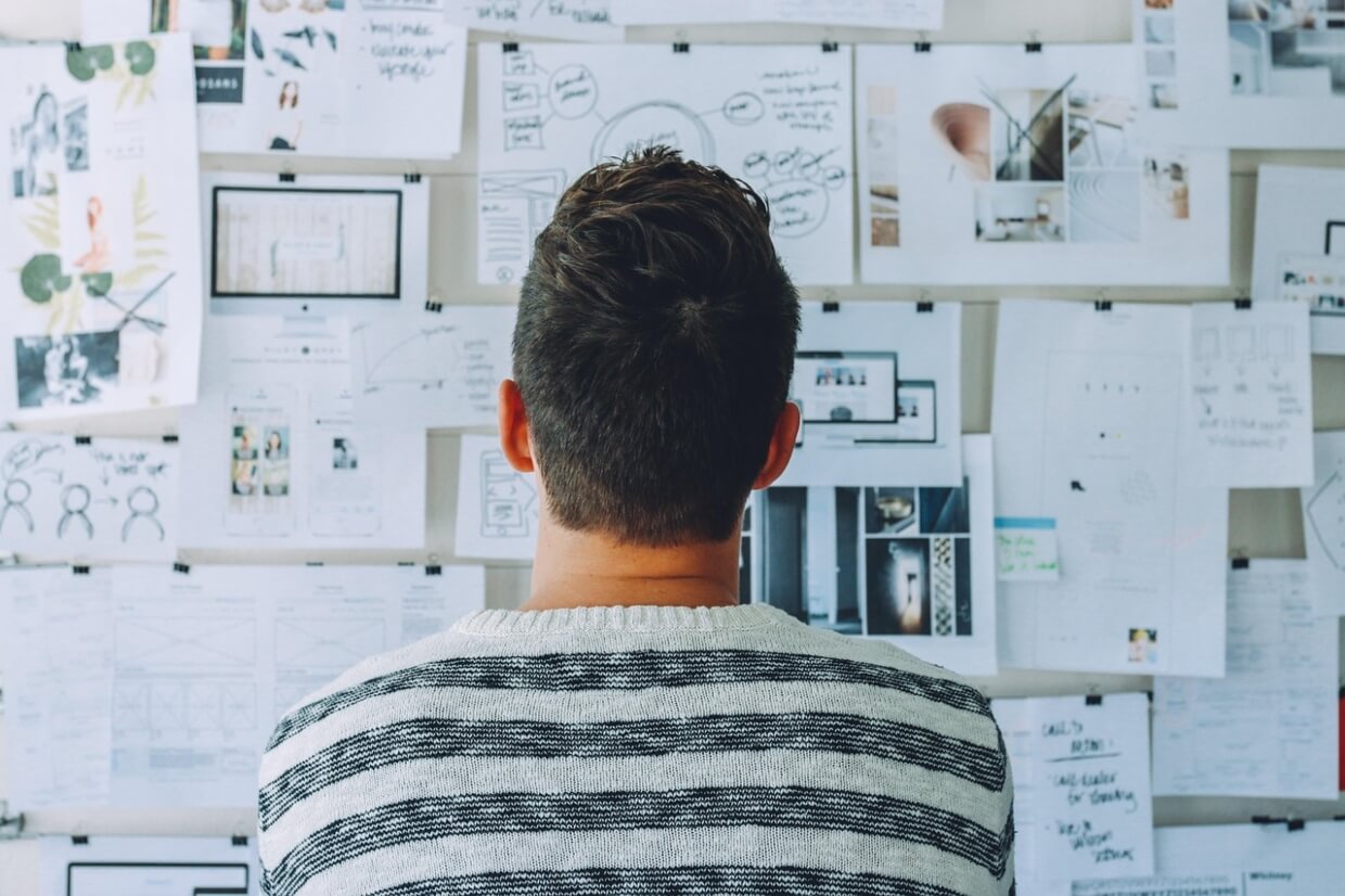 Startup founder studying a research wall covered with wireframes, user personas, and market analysis during product discovery